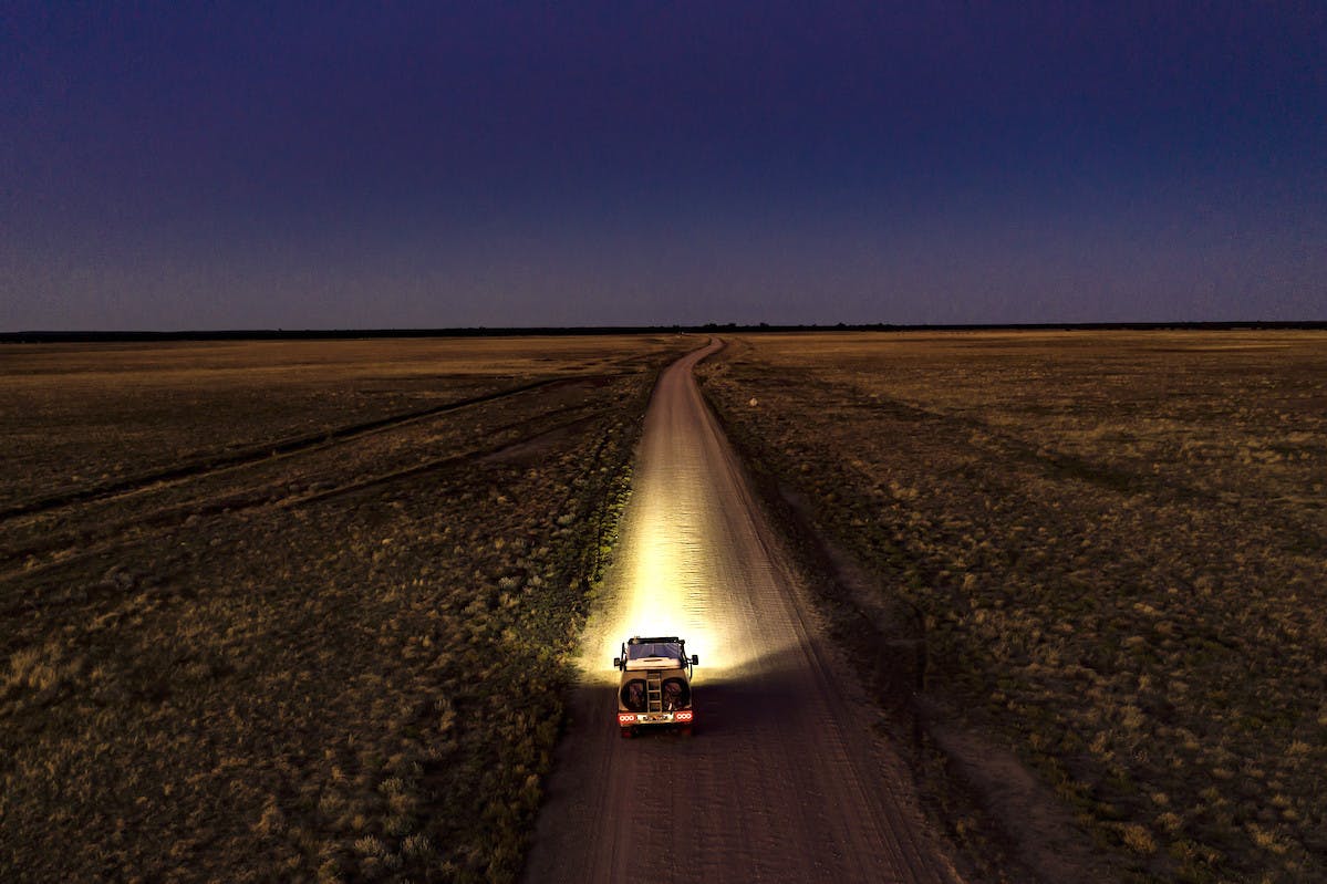 A car drives on a dusty desert road beneath a canopy of stars.